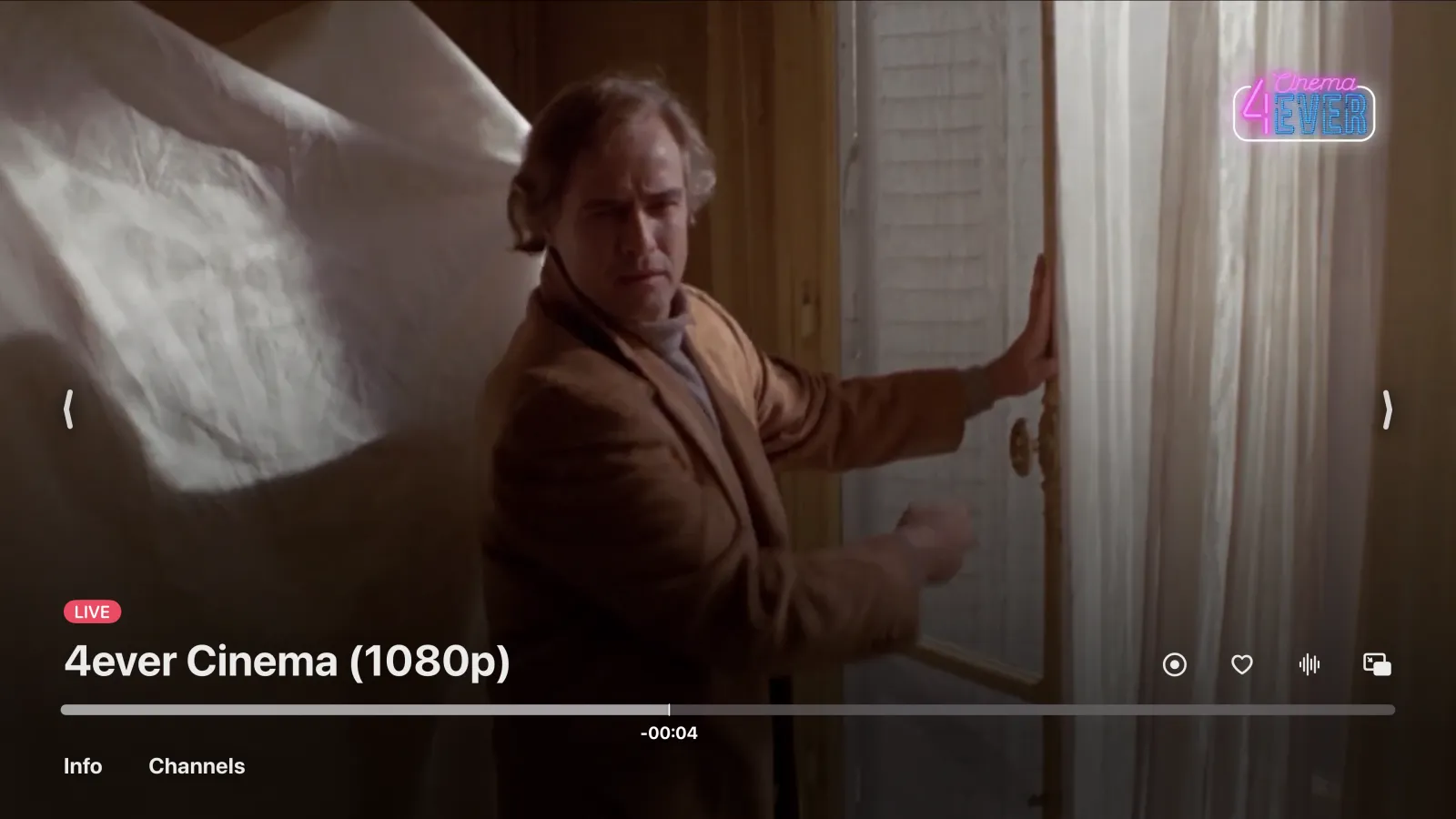 A live channel playing in Tomo TV on Apple TV, with a LIVE badge, the channel name and an arrow at each side of the picture